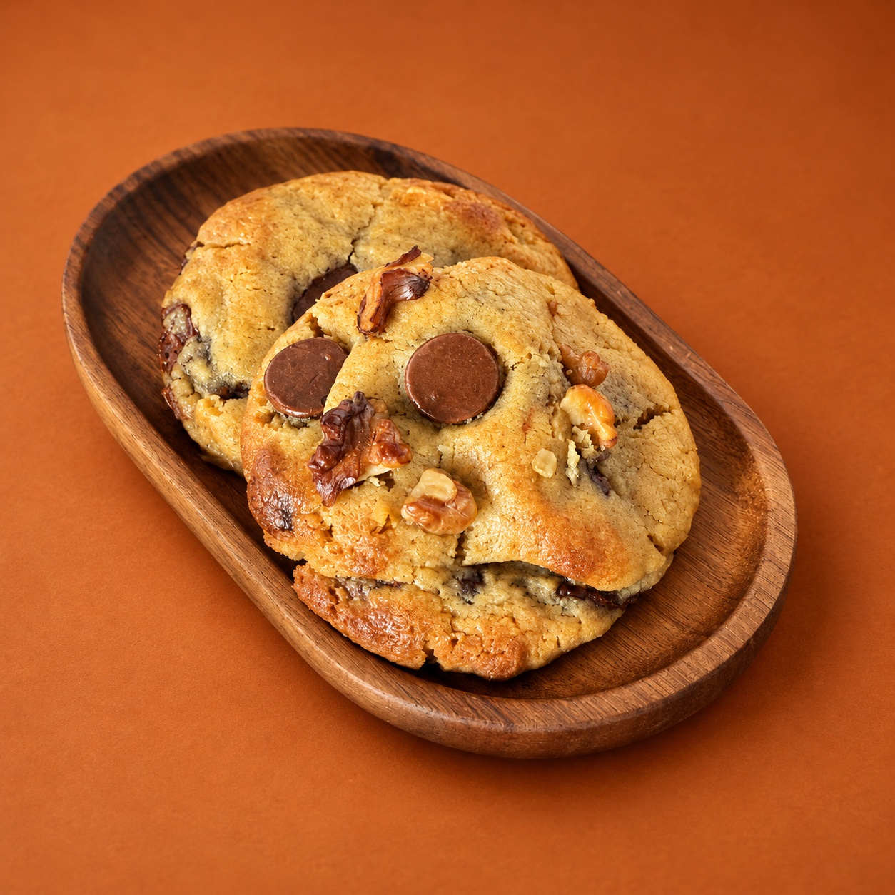 Dos cookies de nuestra producción con chocolate y nueces, en una fotografía retocada sobre fondo naranja